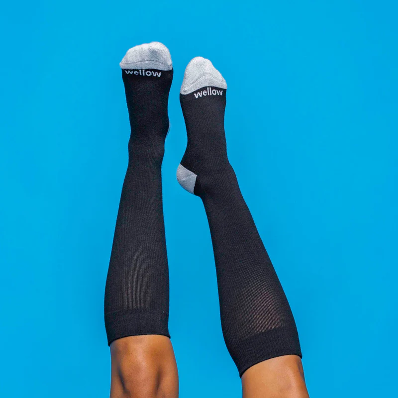 Black Wellow compression socks with grey toes and heels against a blue background