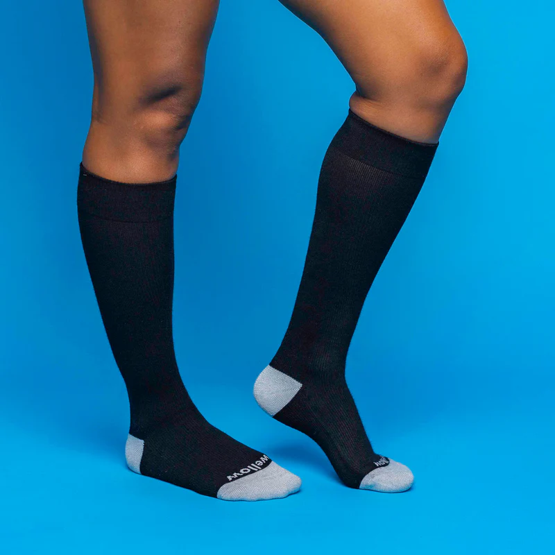 Person wearing black Wellow knee-high compression socks on a blue backdrop